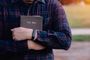 mann im griff und umarmt die bibel auf der bank. christliches beten glauben konzept. foto