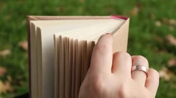 Mädchen, das ein Buch im Herbstpark liest. weibliche hände öffnen an einem warmen sonnigen tag die seiten eines papierbuches im freien. Der Student bereitet sich auf die Prüfung vor. Literarische Freizeit in der Natur. foto