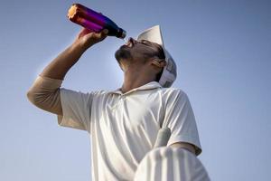 indische cricketspieler im weißen kleid von testspielen, die wasser aus einer flasche auf dem cricketfeld trinken. foto
