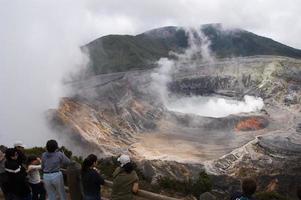 Poas, Costa Rica - 03.08.2007 - Luftaufnahme des Vulkans Poas. Gruppe von Touristen, die auf den Krater schauen, während Rauch austritt. foto