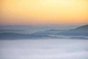 Nebeliger Landschaftswald am Morgen schöner Sonnenaufgangnebel bedeckt Berghintergrund im Landschaftswinter. foto