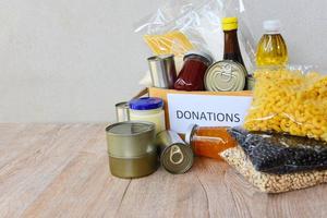 Spendenbox mit Konserven auf Holztisch Hintergrund Pasta Konserven und Trockenfutter unverderblich mit Erbsen Speiseöl Reisnudeln Spaghetti Makkaroni Spenden Lebensmittel foto
