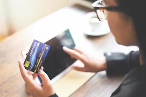 Frauenhände, die Kreditkarte halten und Tablet für Online-Shopping in einem Bürotisch Kaffeetassenhintergrund verwenden - arbeitende Menschen, die Technologie-Geldbörsen-Online-Zahlung zu Hause bezahlen, Kreditkartenmodell foto