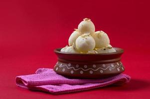 indische Süßigkeit oder Dessert - Rasgulla, berühmte bengalische Süßigkeit in Tonschale mit Serviette auf rotem Hintergrund foto