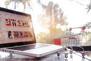 Online-Shopping-Konzept - Einkaufswagen oder Trolley und Laptop auf dem Tisch foto