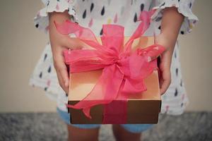 Ein Kind hält eine rote Geschenkbox zum Verschenken in den Ferien. ferien, geschenk, geschenkkonzept. neujahrstag, weihnachtstag, chinesischer neujahrstag, geburtstag. foto