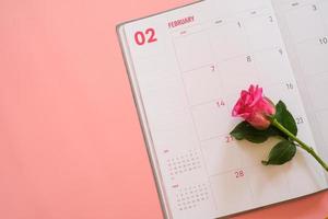 Rosa Rose auf Kalenderbuch isoliert auf rosa Hintergrund mit Copyspace für Text. Vintage-Ton. Valentinstag-Konzept. planung terminplaner, veranstaltung, organisator valentinstag. foto