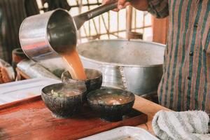 Koch mit Lurik-Uniform gießt eine Suppe in Soto Bathok in Yogyakarta foto