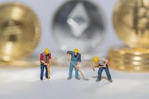 wertvolle kryptomünzen bitcoin ether und ada in einer reihe mit drei arbeitern auf grauem hintergrunddetail foto