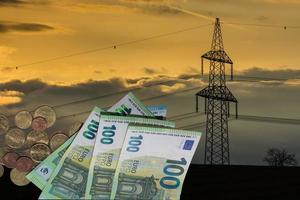 Strommast während des Sonnenuntergangs mit 100-Euro-Scheinen und Münzen bezüglich Strompreiserhöhungen foto