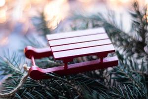 Weihnachtsbaumspielzeug kleiner roter Holzschlitten auf dem Hintergrund eines Weihnachtsbaums und Girlanden foto