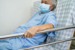 asiatischer älterer oder älterer alter Patient, der eine Maske zum Schutz des Coronavirus trägt, legt sich hin und greift das Schienenbett mit Hoffnung auf einem Bett im Krankenhaus an foto