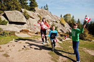 Glücklicher Kanada-Tag. familie der mutter mit drei kindern feiert große kanadische flagge in den bergen. foto