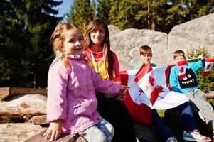 Glücklicher Kanada-Tag. familie der mutter mit drei kindern feiert große kanadische flagge in den bergen. foto