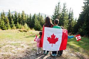 Glücklicher Kanada-Tag. familie der mutter mit drei kindern feiert große kanadische flagge in den bergen. foto