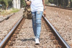 Mädchen, das in der Eisenbahn spazieren geht und zerrissene Jeans trägt, Umhängetasche, weiße T-Shirts, Turnschuhe, Hipster-Stil, lässig, Kleidung für die Jugend, kein Gesicht, Unterkörper, sportlicher Stil. foto