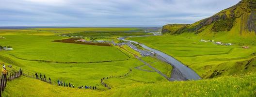 Panoramablick über die Treppe zum Gipfel des berühmten isländischen Skogafoss-Wasserfalls, mit Touristen beim Wandern in Island, Sommer und Campingplatz am Fuß des Wasserfalls. foto