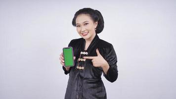 asiatische Schönheit in Kebaya zeigt Smartphone-Bildschirm isoliert auf weißem Hintergrund foto