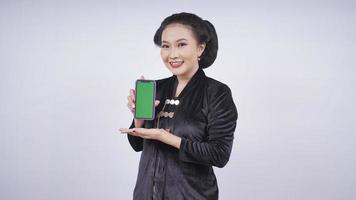 asiatische Schönheit in Kebaya zeigt Smartphone-Bildschirm isoliert auf weißem Hintergrund foto