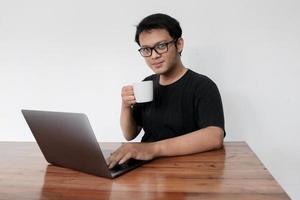 junger asiatischer mann ist ernsthafte arbeit oder denkt vorne am laptop. Indonesien Mann trägt schwarzes Hemd isoliert grauen Hintergrund. foto