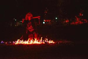 Porträt einer stilvollen blonden Grunge-jungen Frau mit dem Club in der Nähe des Feuers in der Nacht foto