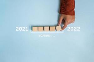 Laden des neuen Jahres 2021 bis 2022 mit der Hand, die Holzwürfel in den Fortschrittsbalken setzt foto