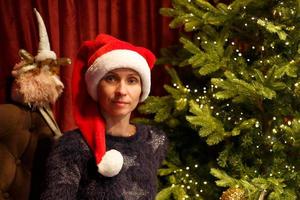 Porträt einer süßen Frau in einem Weihnachtsmann-Hut in der Nähe des Weihnachtsbaums foto