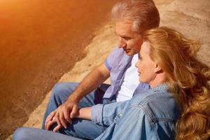 glückliches reifes Paar, das mit seinen Hunden in der Sonne am See sitzt. konzept des familienurlaubs in der natur foto