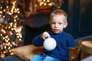 glücklicher kleiner junge, der auf sofa mit weihnachtsbaumdekoration im gemütlichen leben sitzt foto