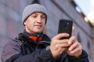 porträt eines glücklich lächelnden kaukasischen mannes mit smartphone auf der stadtstraße gegen foto