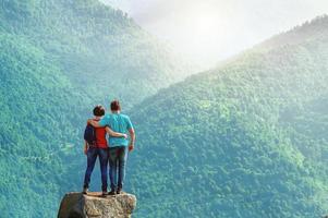 Ein paar Wanderer, die umarmt am Rand der Klippe stehen und einen wunderschönen Morgenblick in die Berge genießen foto