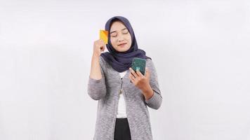 asiatisches Mädchen, das online mit Debitkarten-Denken auf weißem Hintergrund einkauft foto