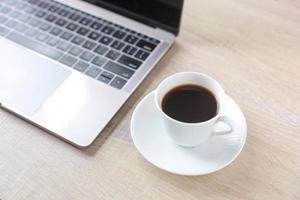eine Kaffeetasse mit Laptop auf dem Schreibtisch aus Holz foto