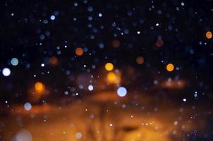 nächtlicher fallender Schnee mit einem Bokeh-Effekt vor dem Hintergrund der Lichter der Stadt. foto