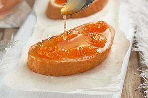 ein Sandwich mit Pfirsichmarmelade auf weißem Holztisch. Brot wird mit Marmelade gegossen. foto