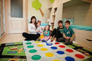 glückliche familie, die zusammen spaß hat, vier kinder und mutter, die zu hause ein twister-spiel spielen. foto