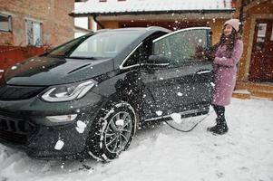 junge Frau, die im Winter ihr Elektroauto auflädt. foto