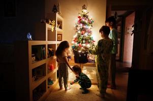 Kinder, die am Abend nach Hause auf den Weihnachtsbaum mit leuchtenden Girlanden schauen. foto