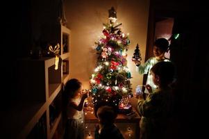 Kinder, die am Abend nach Hause auf den Weihnachtsbaum mit leuchtenden Girlanden schauen. foto