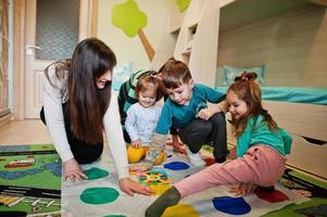 glückliche familie, die zusammen spaß hat, vier kinder und mutter, die zu hause ein twister-spiel spielen. foto