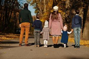 große Familie mit vier Kindern, die sich an den Händen halten und im Herbstpark auf der Straße stehen, Rückansicht. foto