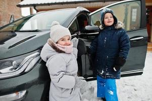 kinder, die im winter ein elektroauto im hof des hauses aufladen. foto