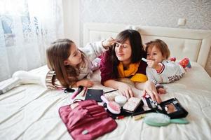 mutter und töchter schminken sich auf dem bett im schlafzimmer. foto