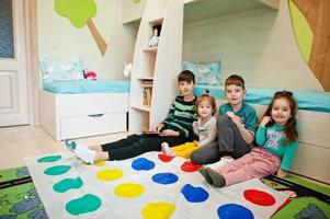 glückliche familie, die zusammen spaß hat, vier kinder, die zu hause ein twister-spiel spielen. foto