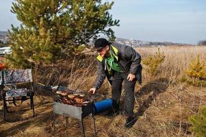 Mann beim Grillen auf einer Terrasse im Pinienwald. Grilltag mit Grill. foto