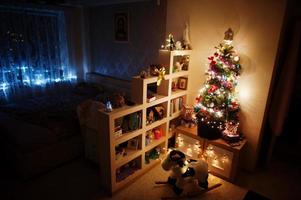 hobby kuh spielzeug gegen weihnachtsbaum mit leuchtenden girlanden am abend nach hause. foto