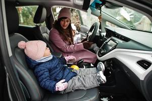 junge mutter mit kleiner mädchentochter sitzt im winter im elektroauto im hof ihres hauses. foto