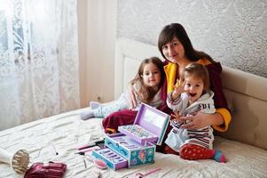 mutter und töchter schminken sich auf dem bett im schlafzimmer. foto