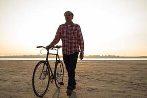 Fahrradfahrer, der bei Sonnenaufgang in der Wüste mit schwarzem Retro-Fahrrad spazieren geht foto