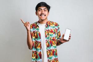 asiatischer mann, der einen leeren bildschirm des smartphones zeigt, der mit hand und finger zur seite zeigt foto